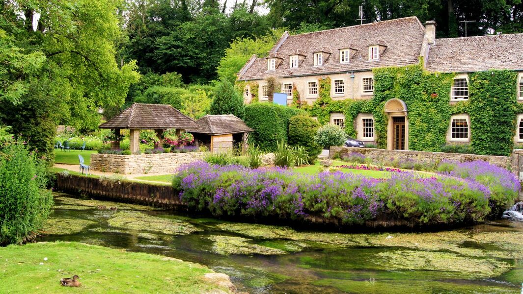 Traditional Cotswolds village scene with stone cottages, landscaped garden and stream in the English countryside